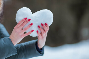 Woman holds heart made from snow. Manicure red nails
