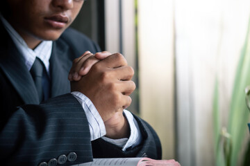 Close up hands of christian man in a suit praying on desk.