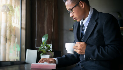 Man in a suit reading Bible and holding coffee cup.