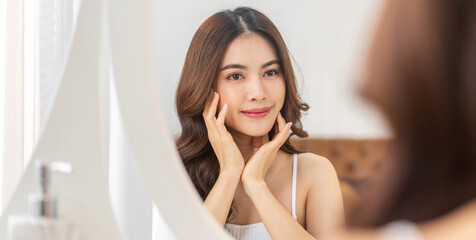 Smiling of young beautiful pretty asian woman clean fresh healthy white skin looking at mirror.asian girl touching on her face with hand and applying cream at home.spa and beauty concept © Art_Photo