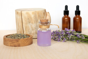 Obraz na płótnie Canvas Dry lavender flowers in wooden bowl and bottle of essential lavender oil or infused water on white background. Natural organic ingredients for herbal cosmetics. Spa massage set, lavender product