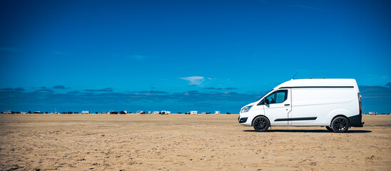 White camper at the beach at a sunny summer day with blue sky and other vans in the background