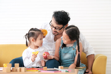 Father teaches kids to eat fruits and is glad that kids eat fruits.