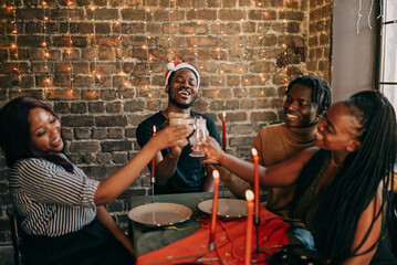 Best friends celebrating new year. Young people with candles, sitting at dining table. Diverse students during christmas party at home, smiling and laughing.