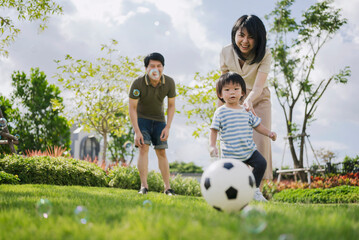 Asian parents and little boy playing soccer in the park together. Happy family life concept.