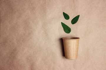 Eco-friendly coffee to go cup with green leaves on brown paper background.