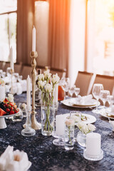 White candles in candelabra and white roses in glass vase on the wedding table decoration. 