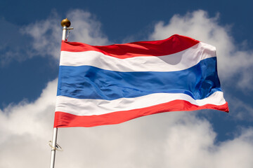 Fototapeta na wymiar The flag of Thailand flies against a clear blue sky with white clouds. Close-up, perfect for news