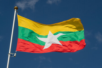 Fototapeta na wymiar The national flag of Myanmar flies against a clear blue sky with white clouds. Close-up, perfect for news