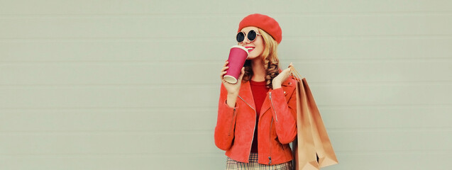 Autumn portrait of beautiful happy smiling young woman with shopping bags and cup of coffee wearing red jacket, beret on gray background