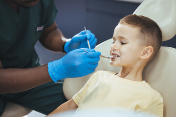 Dentist doing regular dental check-up to little boy. Close up of boy having his teeth examined by a dentist. Cute boy smiling while teeth exam . 