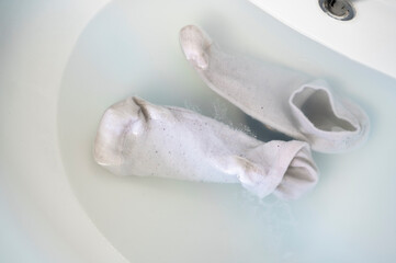 Cleaning dirty socks in the sink water with detergent.