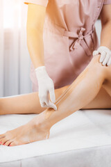 Close up hair removal at spa studio. Young womans legs wax with shugaring.