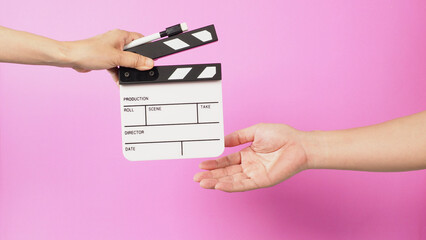 Hand is holding clapper board and marker pen and sending clapperboard to ather hand on pink background.