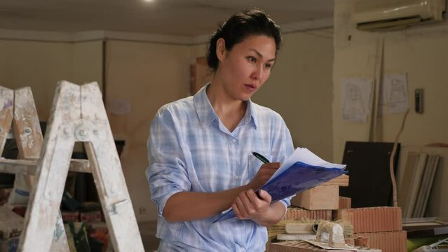 Asian woman takes important notes on a tablet, controlling the process of repair work on a construction site indoors. 