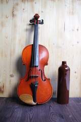 Vintage violin and ceramic brown bottle on wooden background
