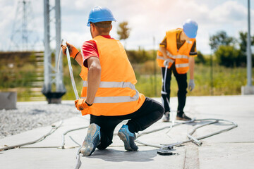 Young electricians prepare an iron thick wire before installation at modern power plant