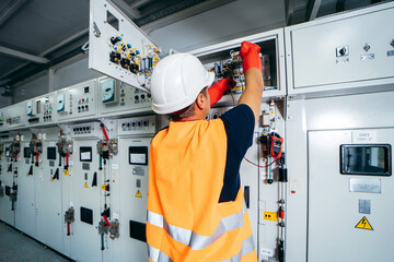 Adult electrician builder engineer testing and screwing equipment in fuse box and repairing of modern electricity power station using voltmeter. Automatic control cabinet