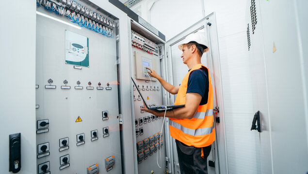 Adult electrician builder engineer testing and screwing equipment in fuse box and repairing of modern electricity power station. Automatic control cabinet