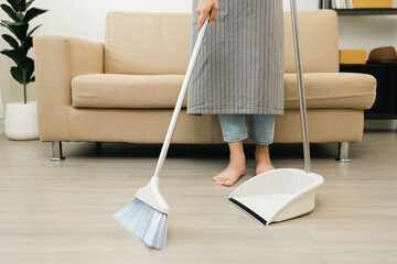 Close up housewife using broom and dustpan wearing an apron to clean the living room at apartment....