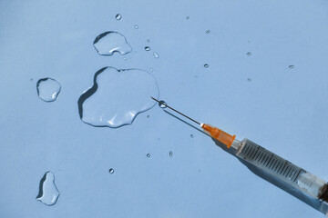 Drops of a transparent liquid and a sterile medical syringe on a blue background. Flat lay, place for text.