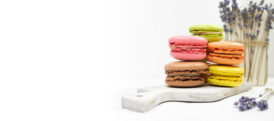 Colorful macaroons on a white wooden board and a bouquet of dried lavender. Banner, flat lay, place for text.