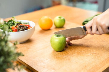 Hand of slicing and cooking green apple on cutting board for vegetable salad in weight loss diet. Beautiful woman happily cooks a healthy breakfast in kitchen in the morning. Diet food concept.