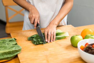 Female slicing and cooking green apple on cutting board for vegetable salad in weight loss diet. Beautiful woman happily cooks a healthy breakfast in kitchen in the morning. Diet food concept.