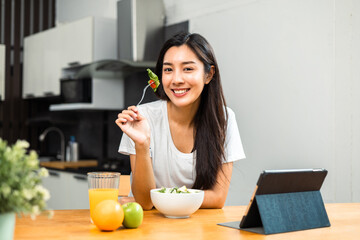 Obraz na płótnie Canvas Young female eating organic greens vegetable salad in weight loss diet and wellness on table. Beautiful woman happily eat a healthy salad breakfast in kitchen in the morning. Diet food concept.