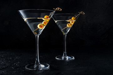 Martini, two glasses with spicy olives, on a black background. Cold drinks