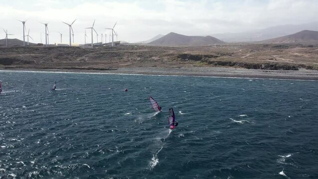 Professional windsurfers training in Tenerife. Fast windsurfing action captured by drone in 4K, 48fps (slow motion optional). Windsurf foiling race gybes. Extreme water sports in strong winds.