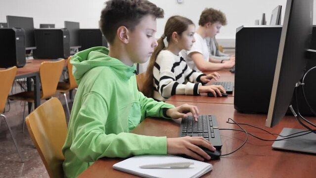 Smart focused tween boy studying with classmates in modern computer lab at school
