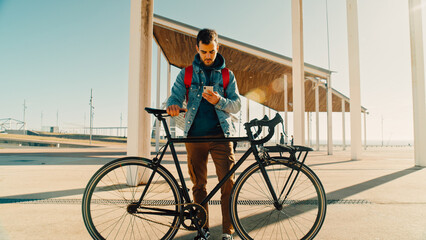 Portrait of handsome millennial generation z young man in cool hipster clothes outfit stand with his commuter city bike in direct sunlight, look into camera, smile confident and happy