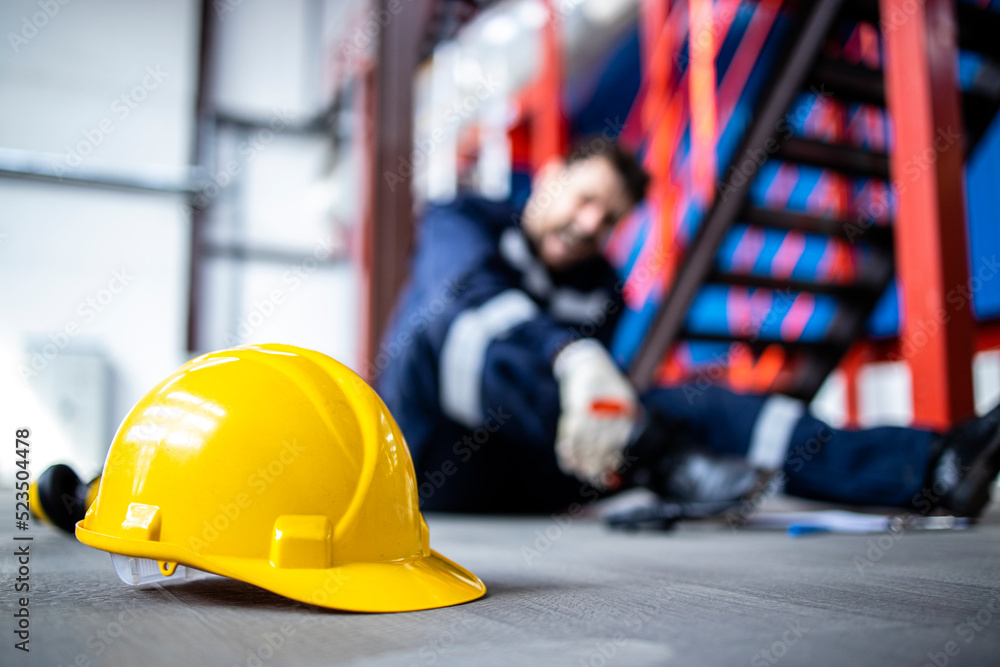 Wall mural Safety at work. Close up view on hardhat and injured factory worker in background.