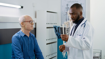 Male doctor showing radiography results to senior man in medical office, analyzing x ray scan...