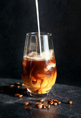 Iced coffee and pouring milk in a glass on a dark background