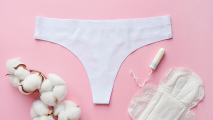 Composition of women's underpants, a branch of cotton, a tampon and a sanitary pad on a pink...