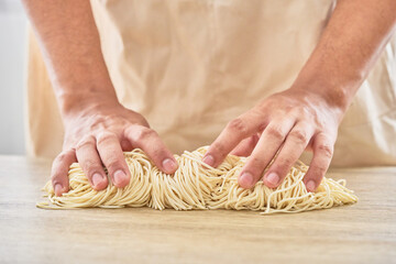 asian man hand kneading raw ramen noodle in wood plate on wooden table background. fresh egg ramen...