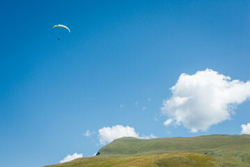 Un parapente dans les Alpes. Un parapentiste au dessus d'une montagne. Un parapente dans un ciel bleu avec un nuage blanc.