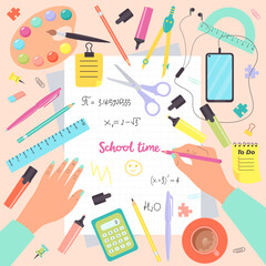 Top view of desk with human hands writing in notebook and school supplies. School time. Colorful set of school objects arranged on a desk from top view.