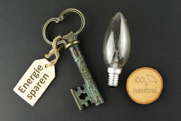 Ein Schlüssel mit einem Schlüsselanhänger auf dem Energie sparen steht, eine Glühlampe und ein CO2 neutral Schild als Symbol für die Lösung zur Nachhaltigkeit, CO2  und Geld einzusparen
