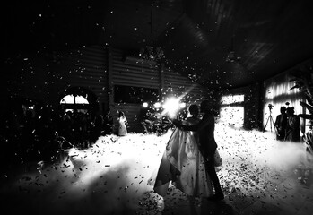 Black and white photo of the first dance of newlyweds with lighting effects and confetti, silhouettes