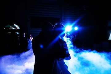Black and blue photo of the first dance of newlyweds with lighting effects and confetti, silhouettes