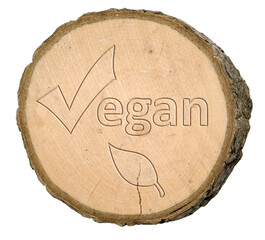 Tree disc or tree slice with bark on which the word vegan and a leaf can be seen on a white background, isolated