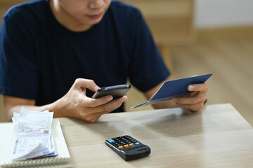 Cropped view of asian man managing household expenses expenditures, paying bills on smart phone