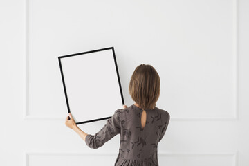 Woman holding blank picture frame mockup on white wall, Artwork mock-up in minimal interior design,...