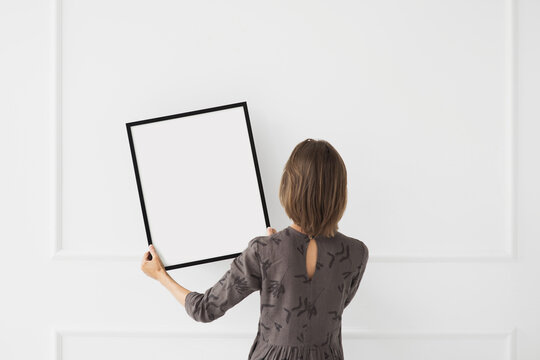 Woman holding blank picture frame mockup on white wall, Artwork mock-up in minimal interior design, Minimal art concept.