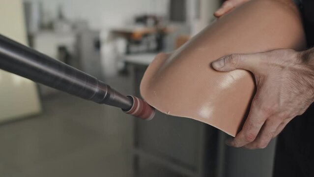 Close-up of unrecognizable man crafting prosthetic leg polishing edges of beige plastic socker detail