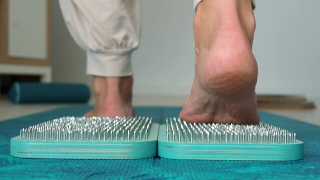 Sadhu wooden blue board with nails, female feet stepping on sharp nails for meditation, leg relaxation, acupuncture tool. Exercises for relaxation and harmonization of the soul, sadhu yoga practice.