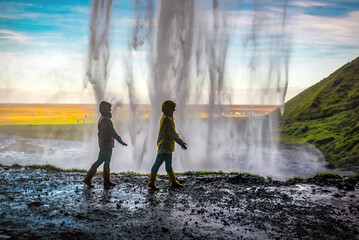 Obraz premium Two women walking under a waterfall Seljalandsfoss in Iceland
